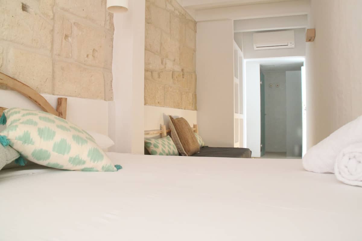 A bedroom with a stone wall, a bed with pillows, and a bathroom door visible.