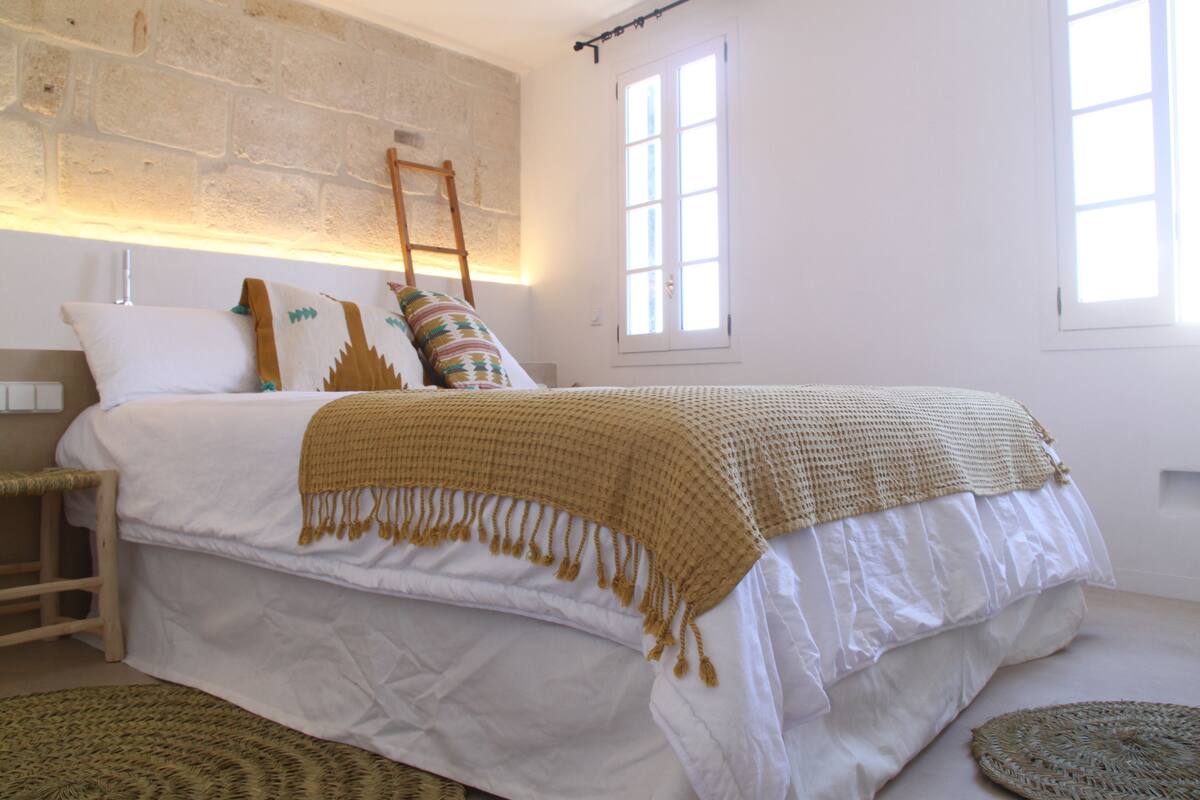 A bedroom with a large bed, a wooden ladder, and a window.