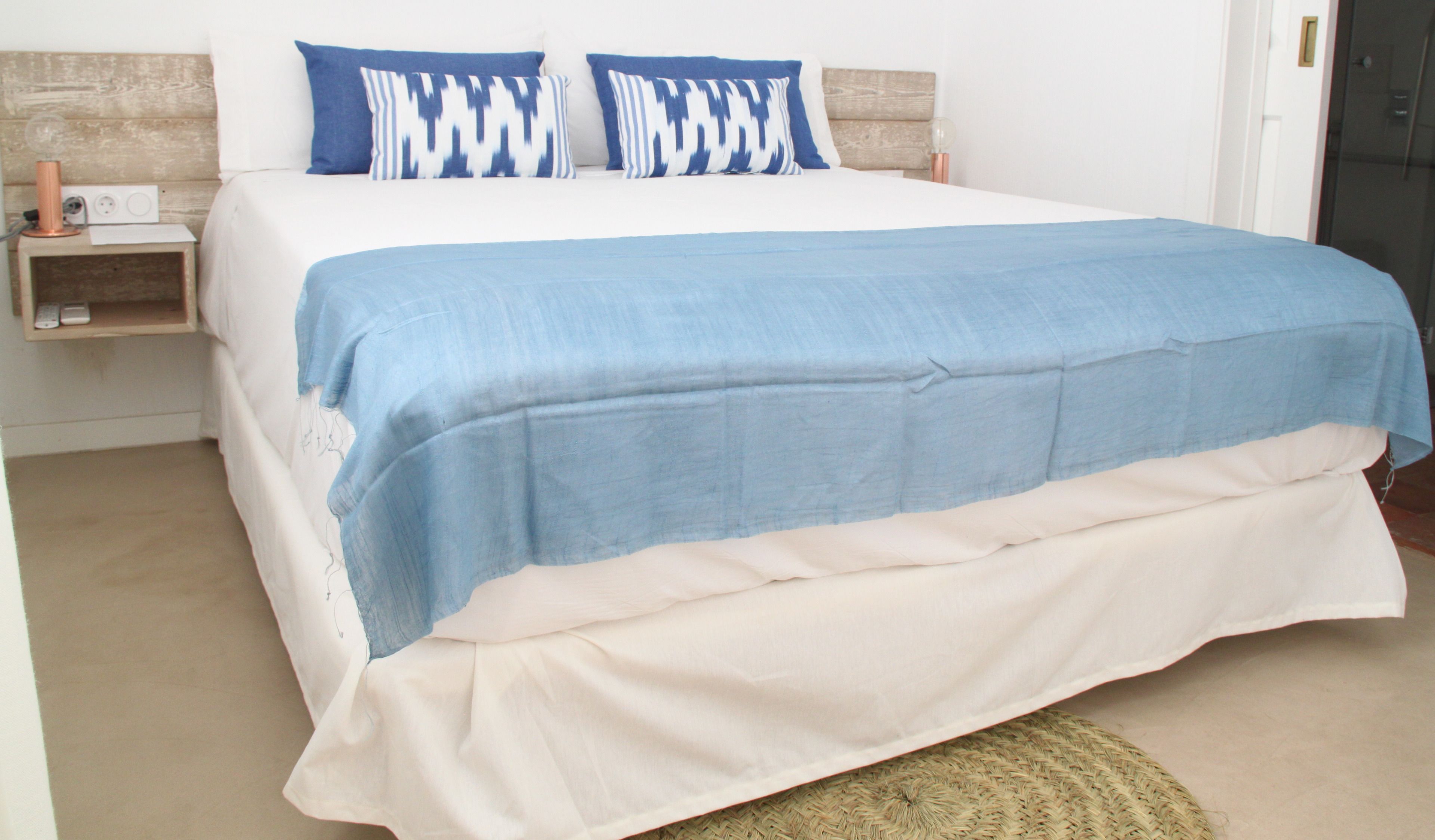 Uma cama com colcha azul e branca, duas almofadas azuis e uma cabeceira de madeira.