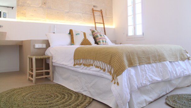 Un dormitorio con una cama grande, una escalera de madera, un taburete pequeño y una alfombra tejida.