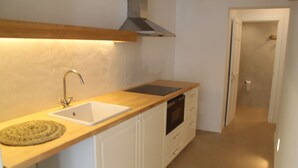 Una cocina con encimera de madera, armarios blancos, campana extractora de acero inoxidable y un lavamanos blanco.
