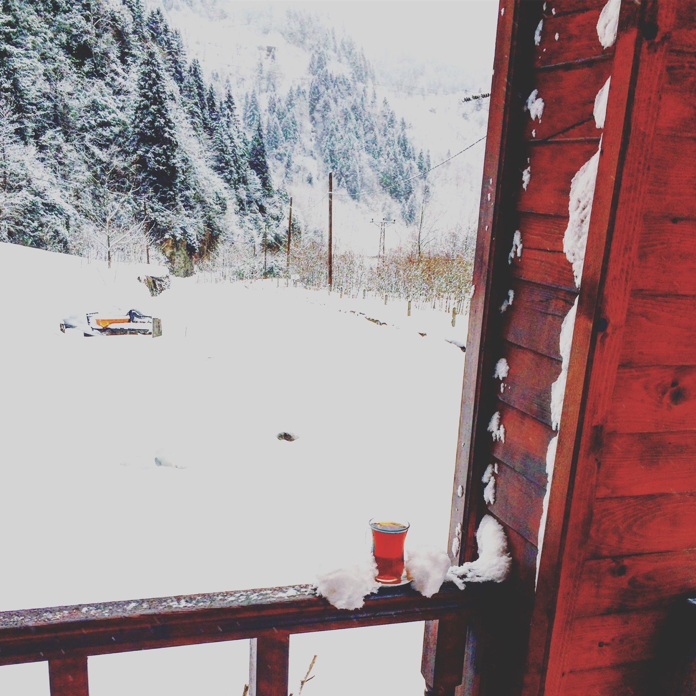 A wooden cabin with a snow-covered deck and a glass of red beverage on it.
