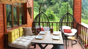 Una terraza de madera con una mesa de comedor dispuesta para cuatro personas, rodeada de sillas de mimbre y un banco acolchado.