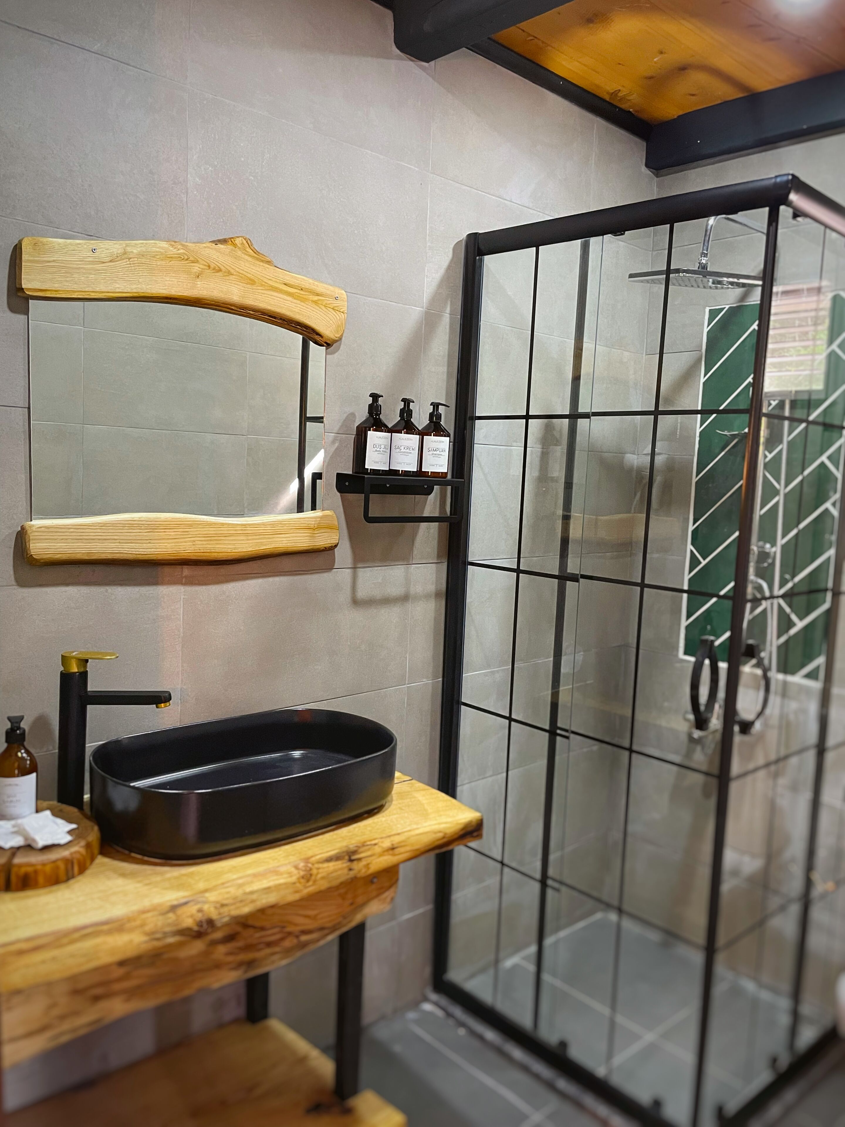 Een badkamer met een houten wastafelmeubel, een zwarte wastafel en een douchecabine met glazen wanden.