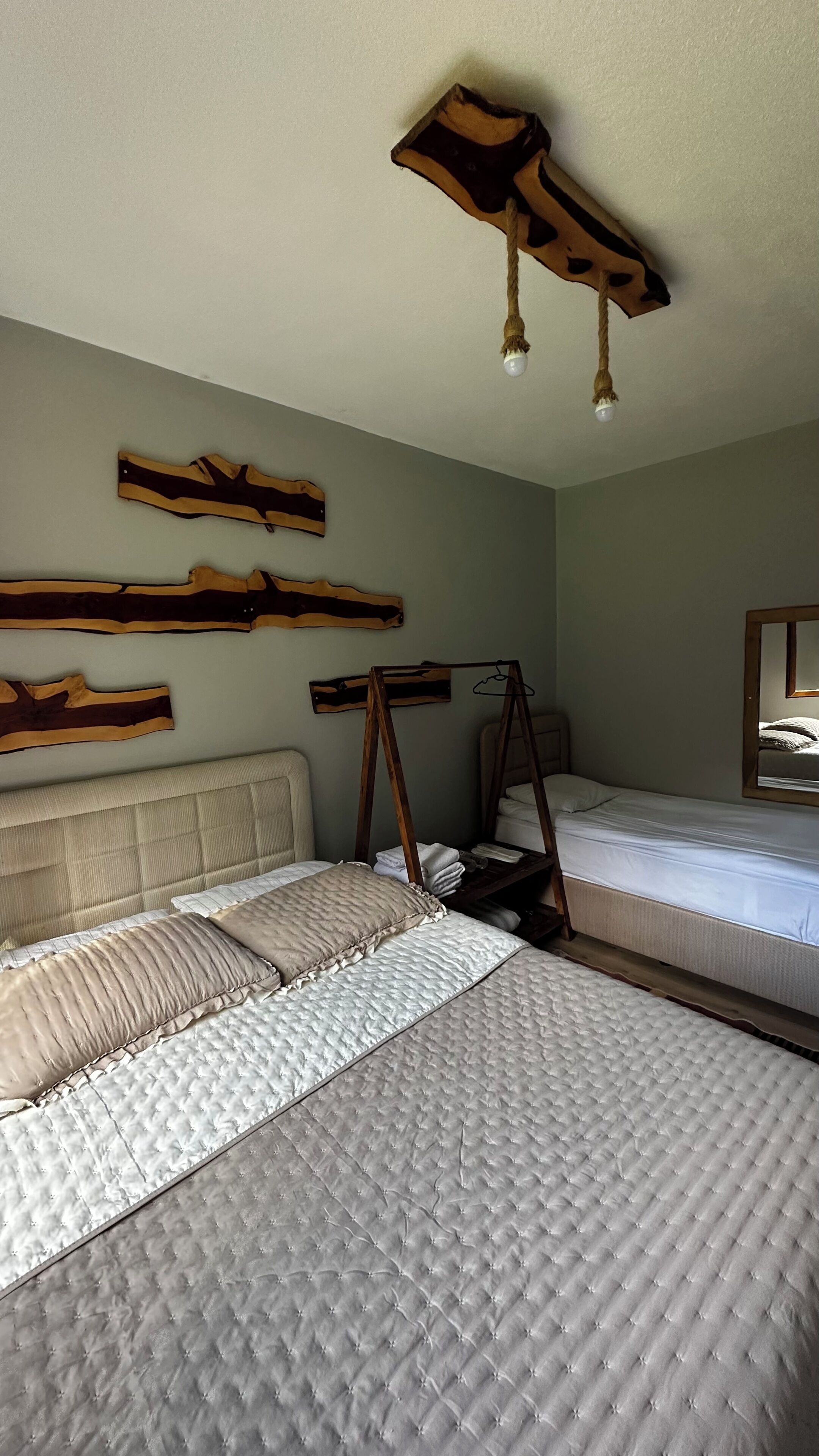 Une chambre avec deux lits, un luminaire en bois au plafond et un miroir sur le mur.