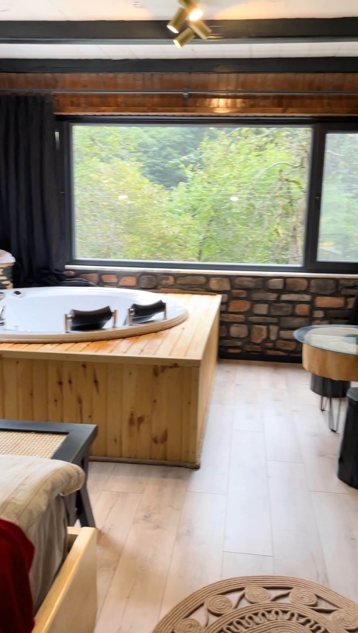 A room with a wooden bench, a small table, and a view of greenery outside.