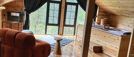 A cozy cabin with a wooden interior, a sofa, a small table, and a view of the outdoors through large windows.