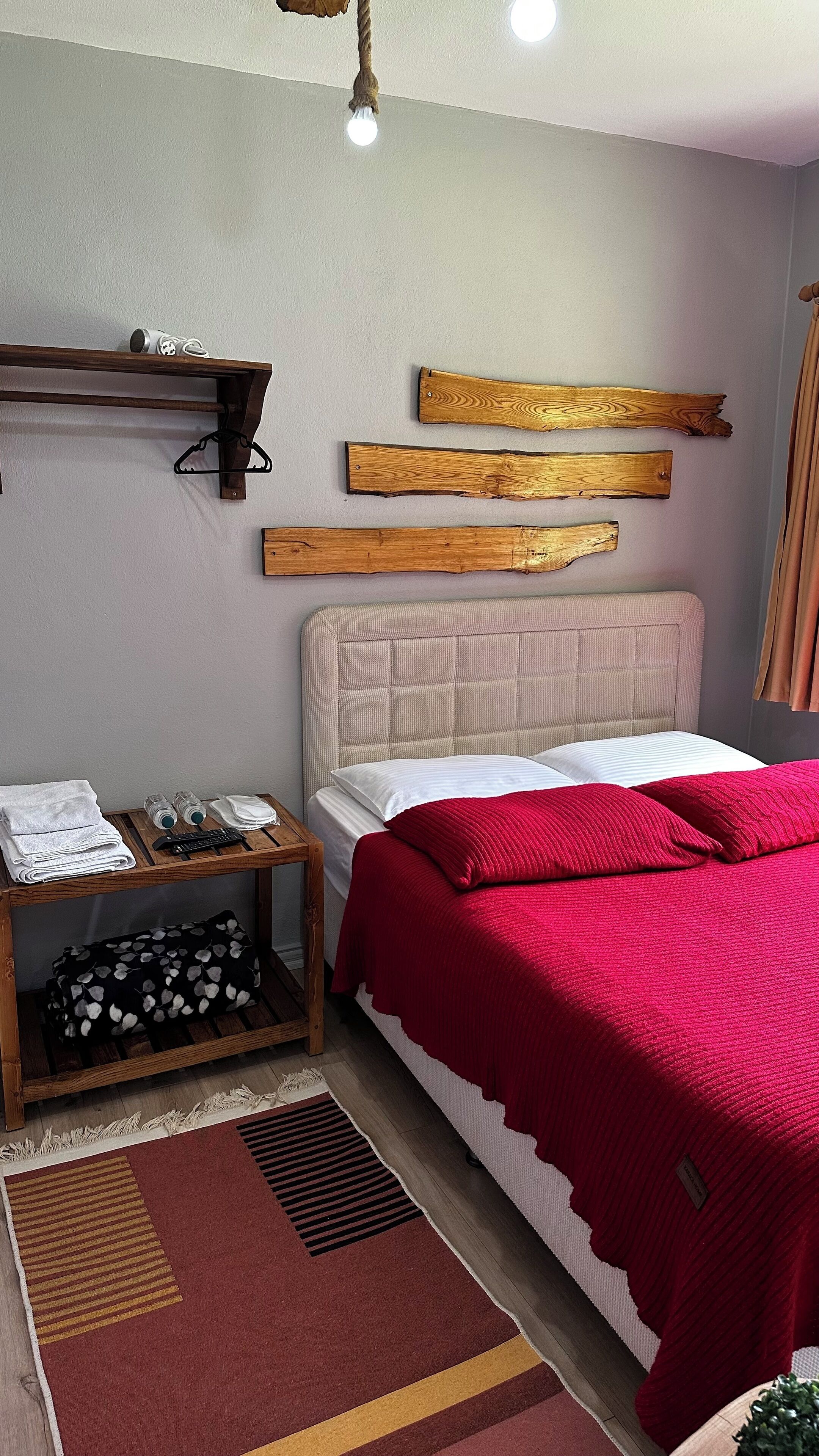 Un dormitorio ordenado con una cama, una mesita de noche, un estante con una toalla enrollada y una lámpara colgante.