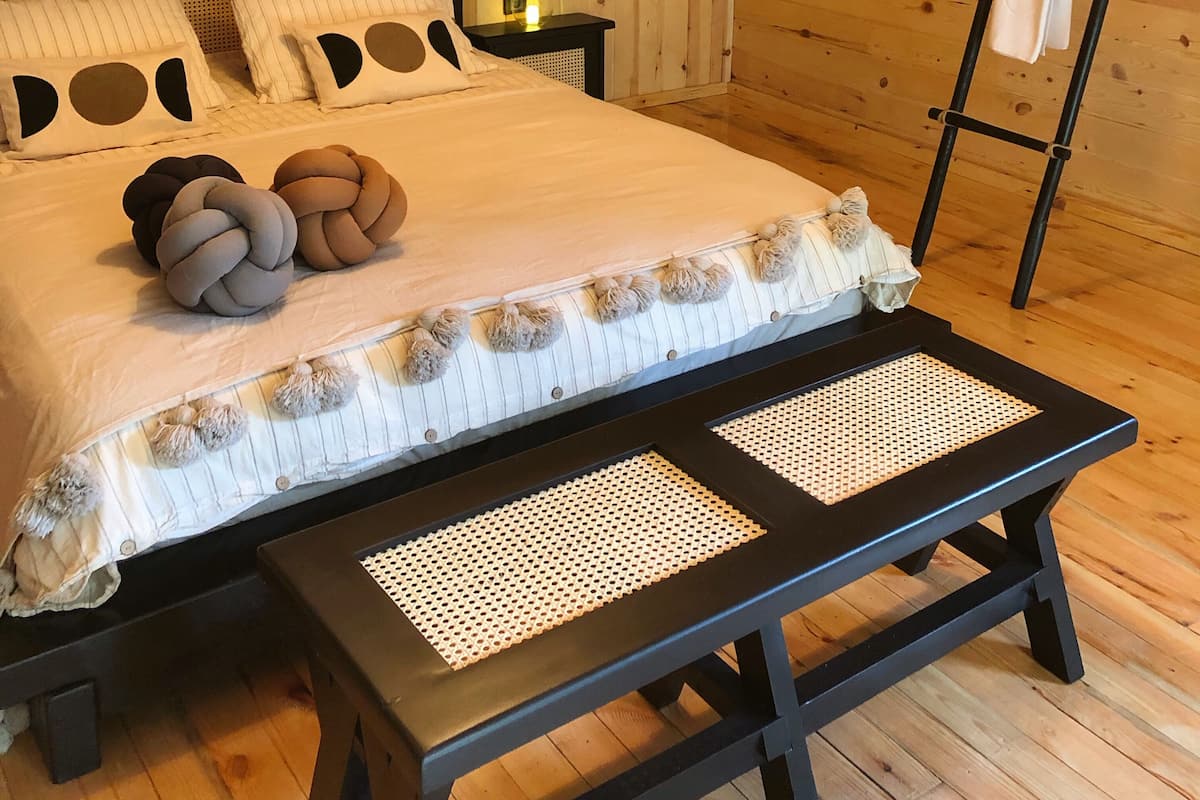 Un dormitorio acogedor de cabaña de madera con una cama, mesitas de noche, una lámpara colgante y una escalera.