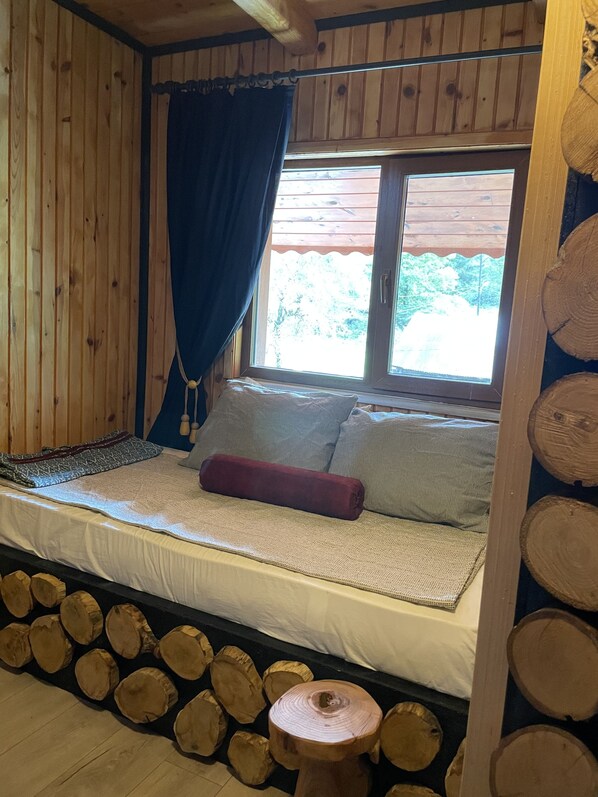 Una habitación de cabaña de madera con una cama, una ventana con cortinas y una pared de troncos.