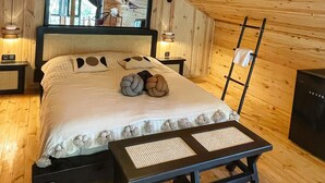 Un dormitorio tipo cabaña de madera con una cama, mesitas de noche, un escritorio y una escalera.