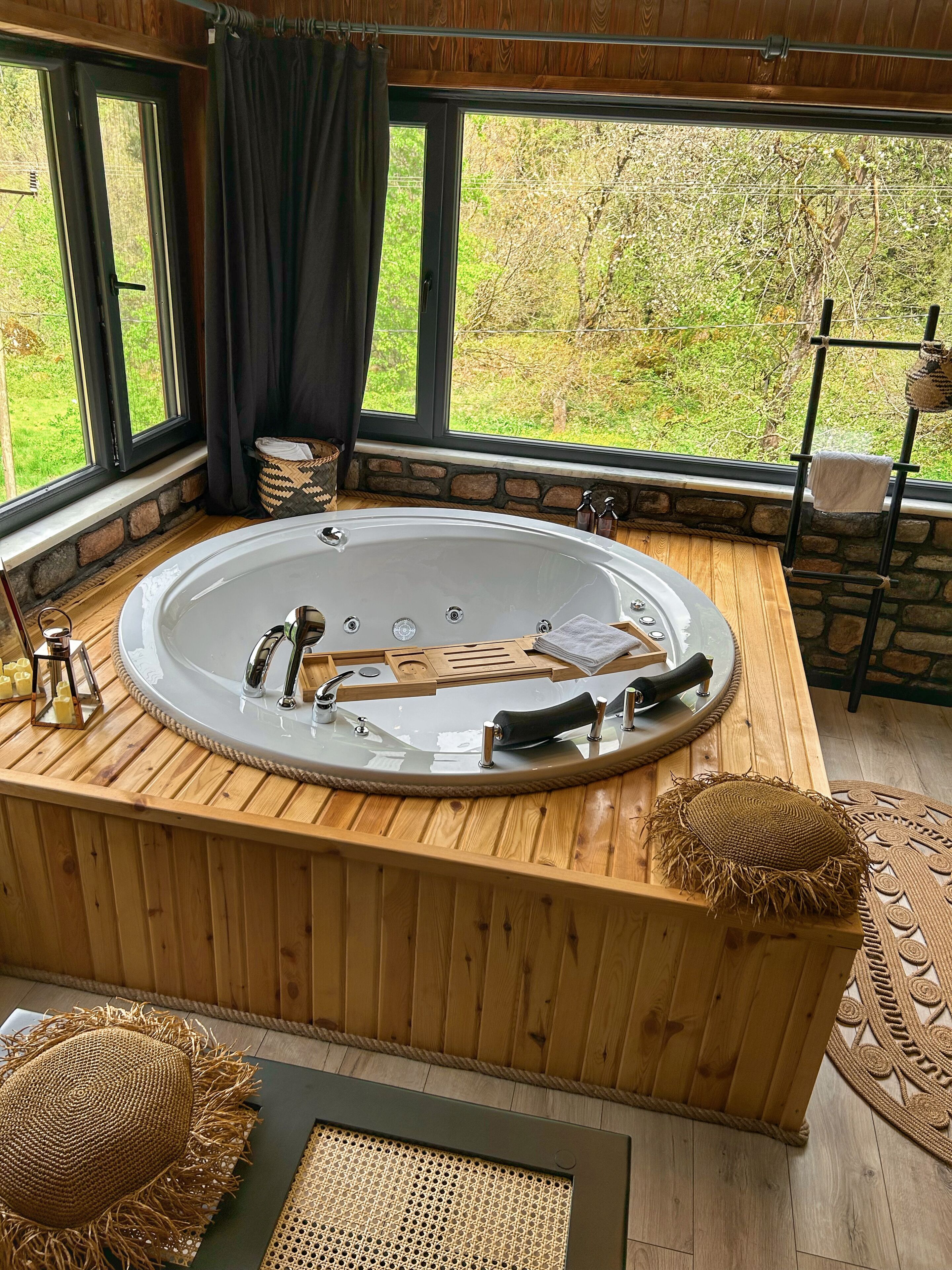 Eine Holzbadewanne mit Steinwand im Hintergrund und Blick ins Grüne.
