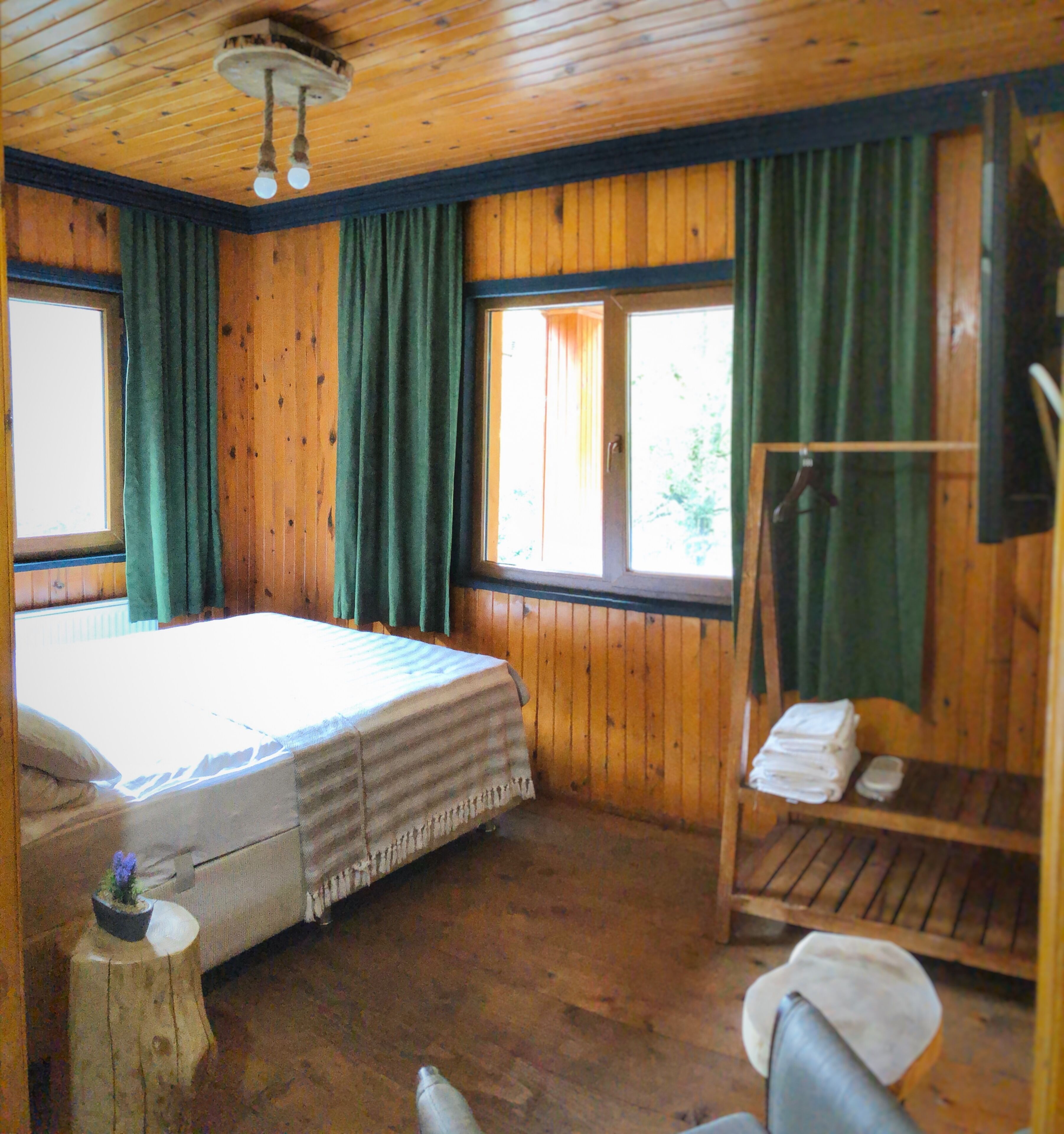 Una stanza in legno con un letto, una panca e una finestra con tende.