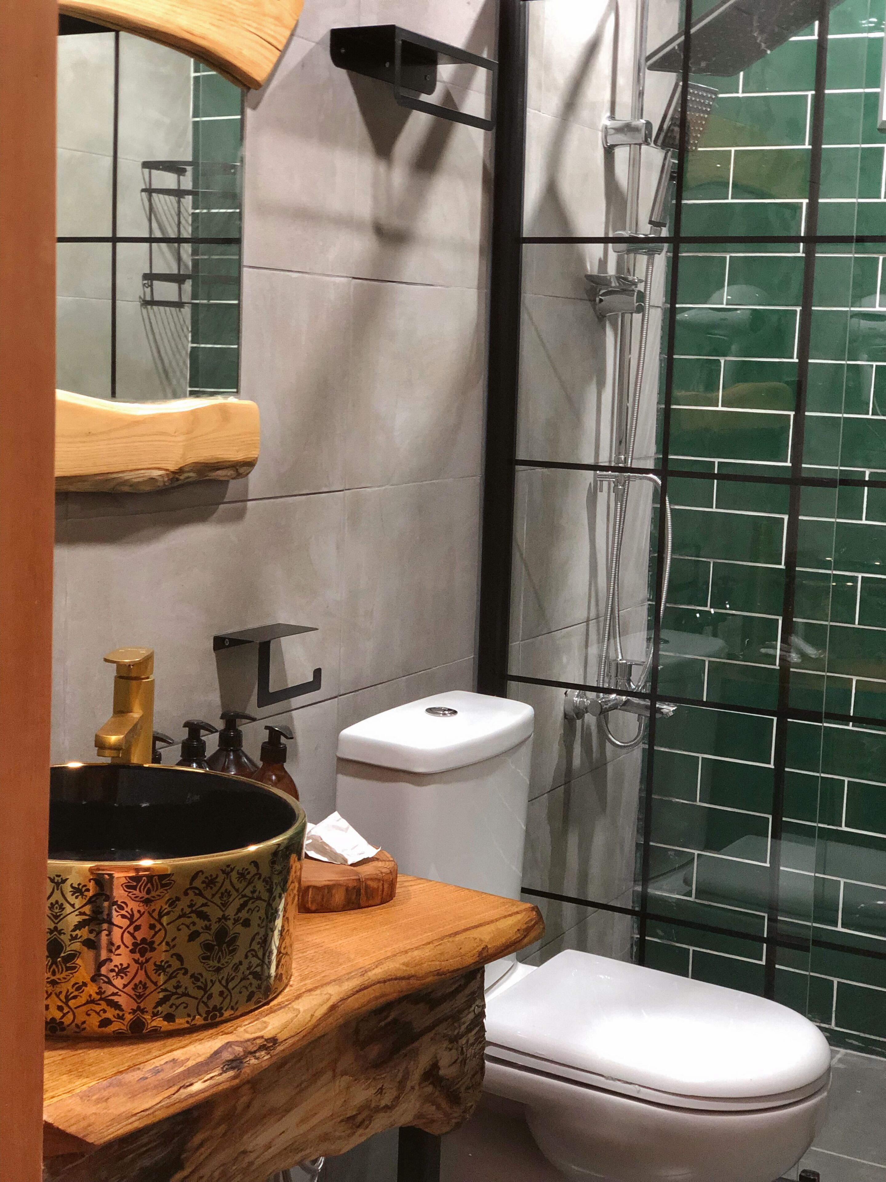 Un baño con tocador de madera, un lavabo con recipiente decorativo, inodoro y zona de ducha con puerta de vidrio.