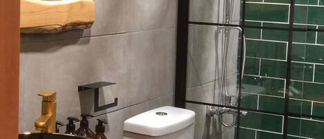 Un baño con tocador de madera, un lavabo con recipiente decorativo, inodoro y zona de ducha con puerta de vidrio.