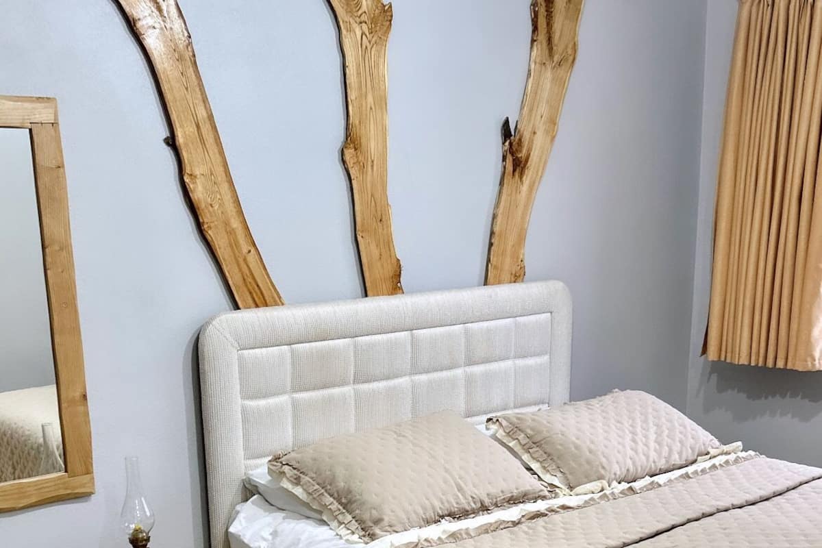 Un dormitorio con una cama grande, un cabecero de madera, un taburete pequeño de madera y un espejo en la pared.