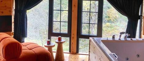 A cozy cabin interior with a wooden floor, a red sofa, a small round table with a cup, and a large bathtub.