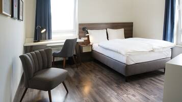 A hotel room with a bed, a desk, a chair, and a window.
