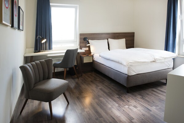 A hotel room with a bed, a desk, a chair, and a window.