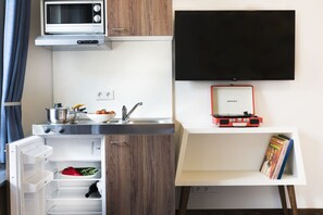 A compact kitchenette with a microwave, stove, sink, and a flat-screen TV mounted on the wall. - KONCEPT Hotel Zum Kostbaren Blut (Cologne)