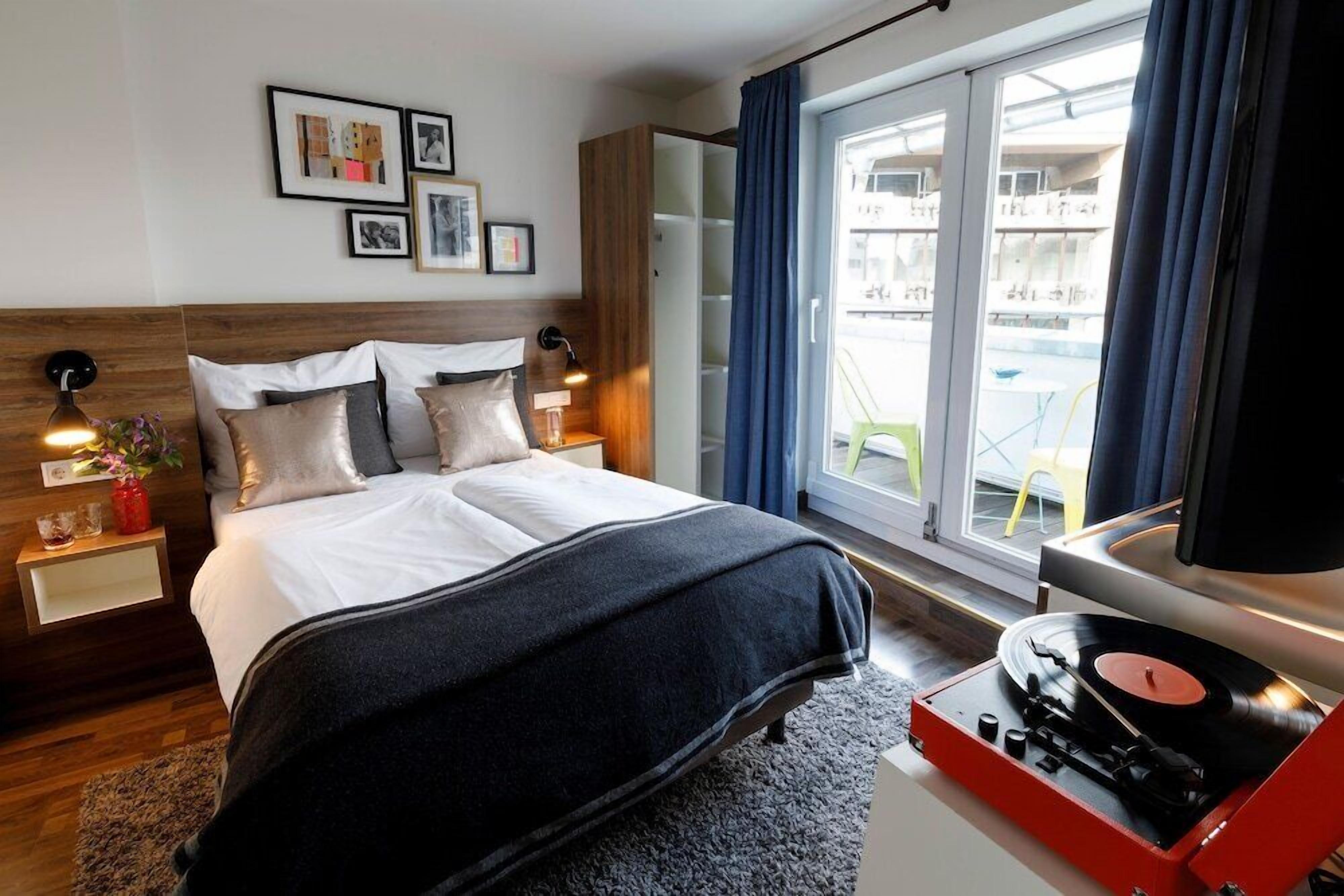 Une chambre d’hôtel moderne avec un grand lit, un tourne-disque et un balcon offrant une vue sur les immeubles.