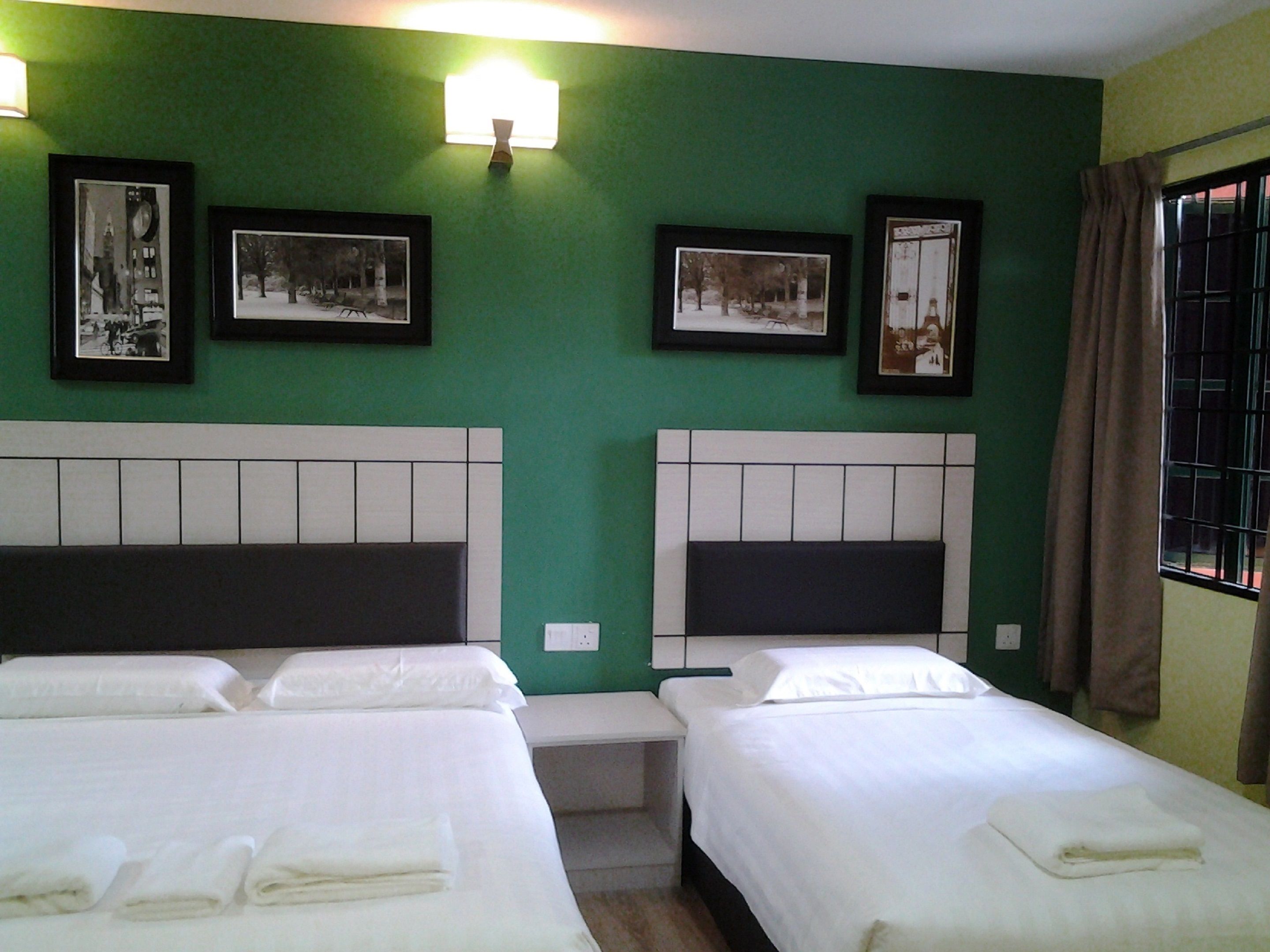 A hotel room with two beds, green walls, and framed pictures on the wall.
