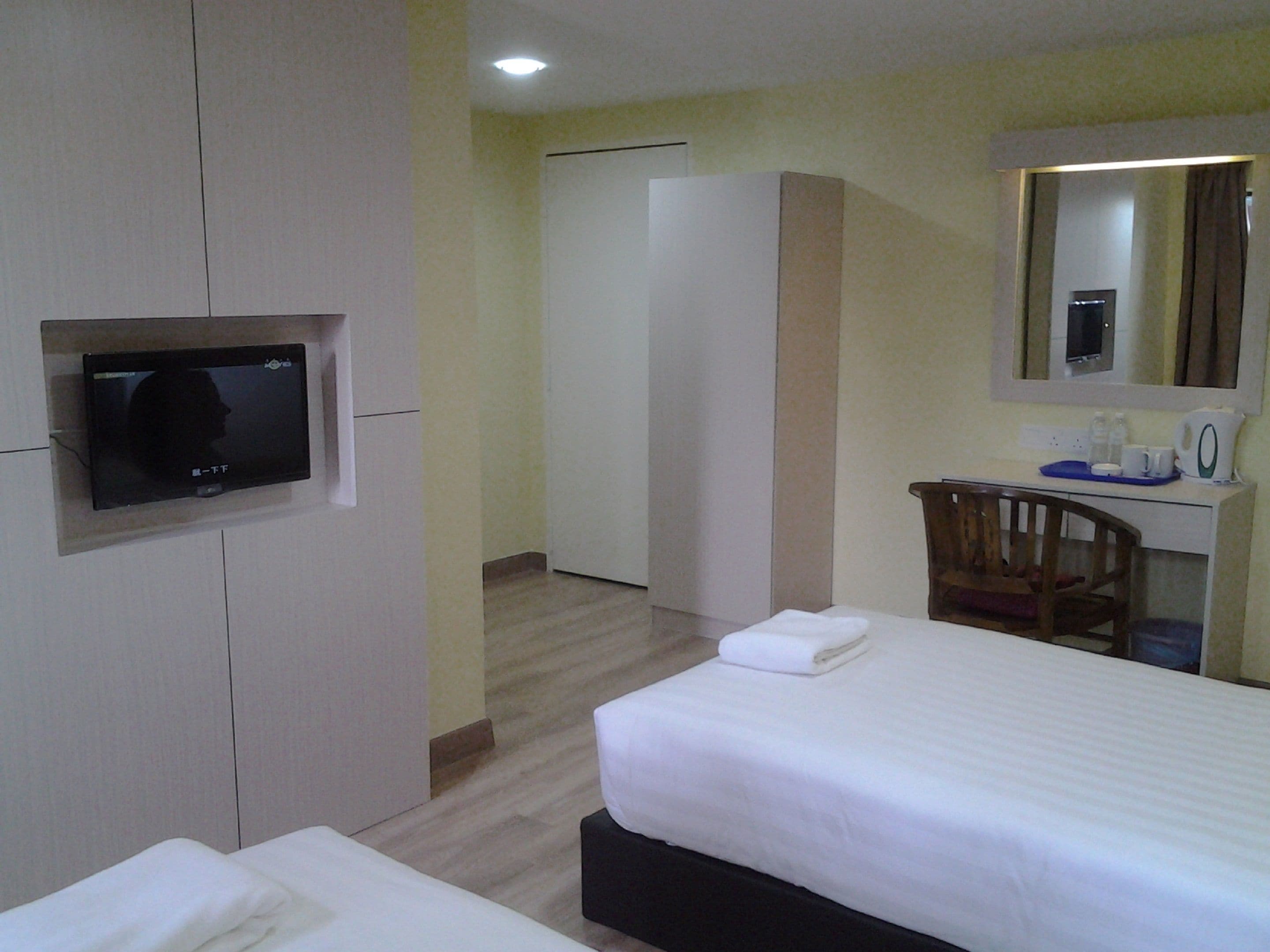 A hotel room with a bed, a TV mounted on the wall, a desk with a chair, and a mirror above the mirror.