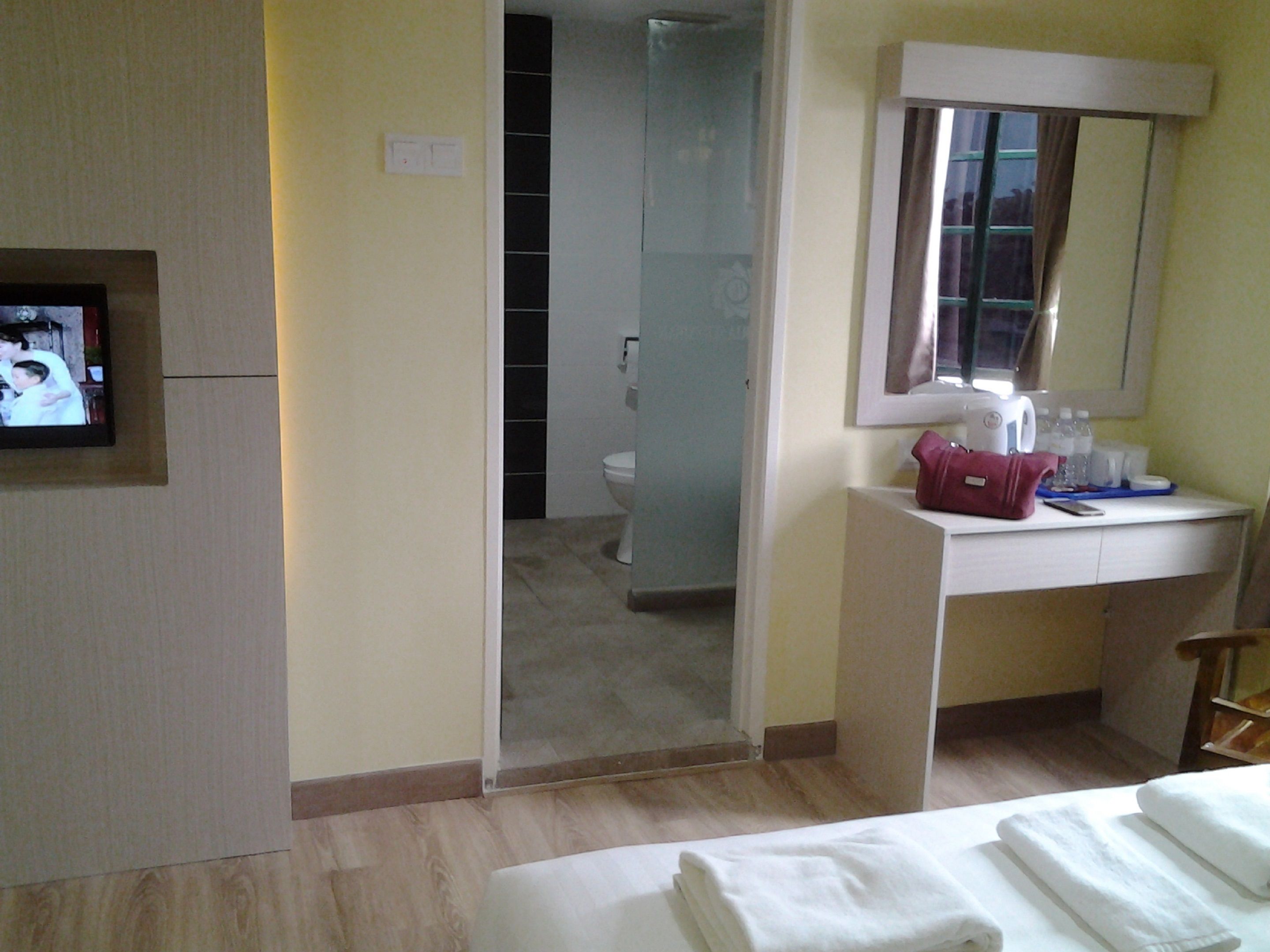 A hotel room with a bed, a bedside table with a mirror, a TV, and a bathroom visible through an open door.