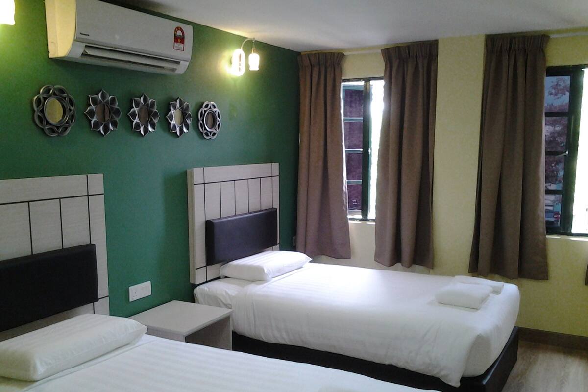 A hotel room with two beds, a wall-mounted air conditioner, decorative wall art, and a window with curtains.