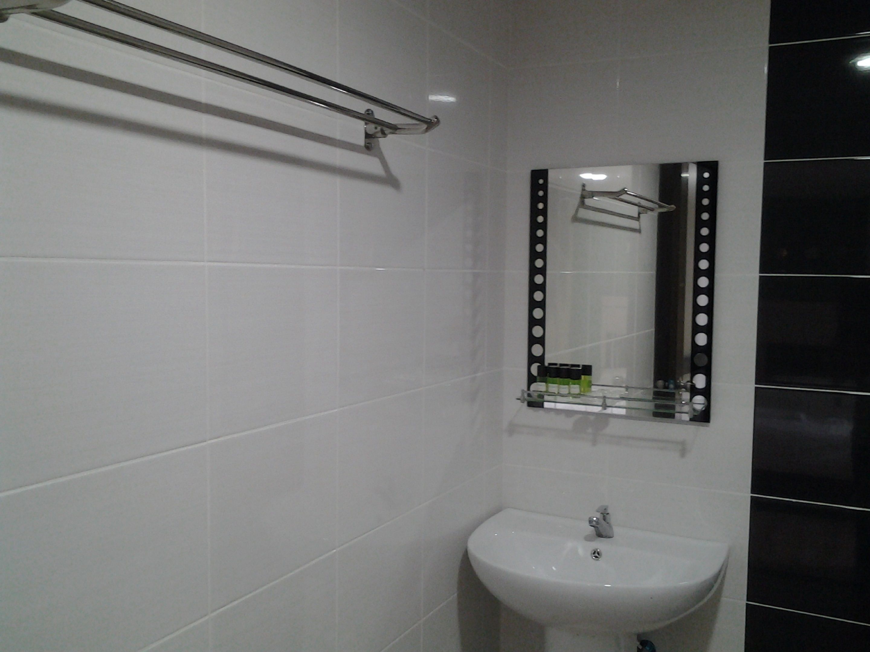 Casa de banho com azulejos brancos, lavatório branco e espelho com moldura preta.