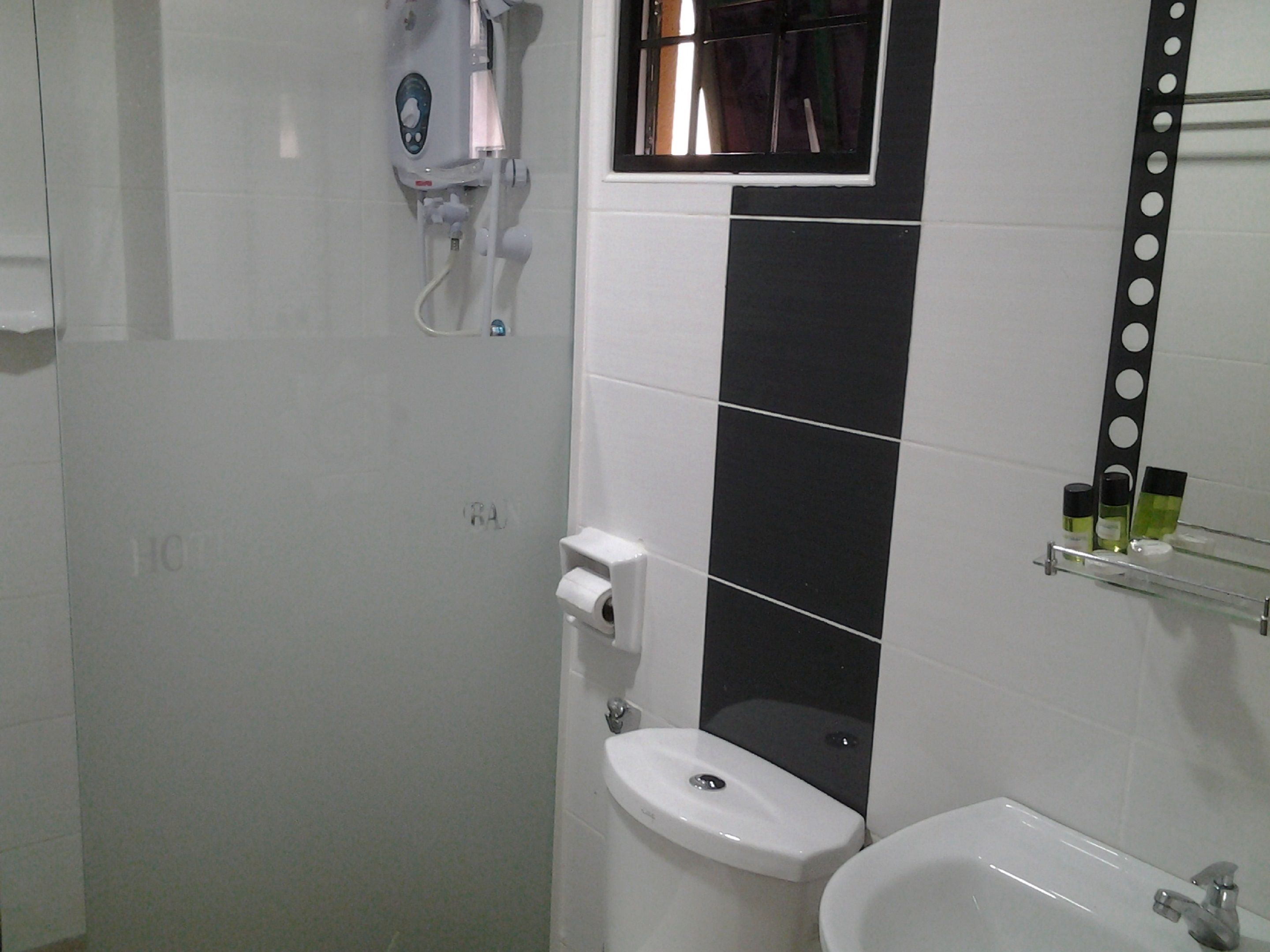 A bathroom with a toilet, sink, and a mirror with a black tile backsplash.