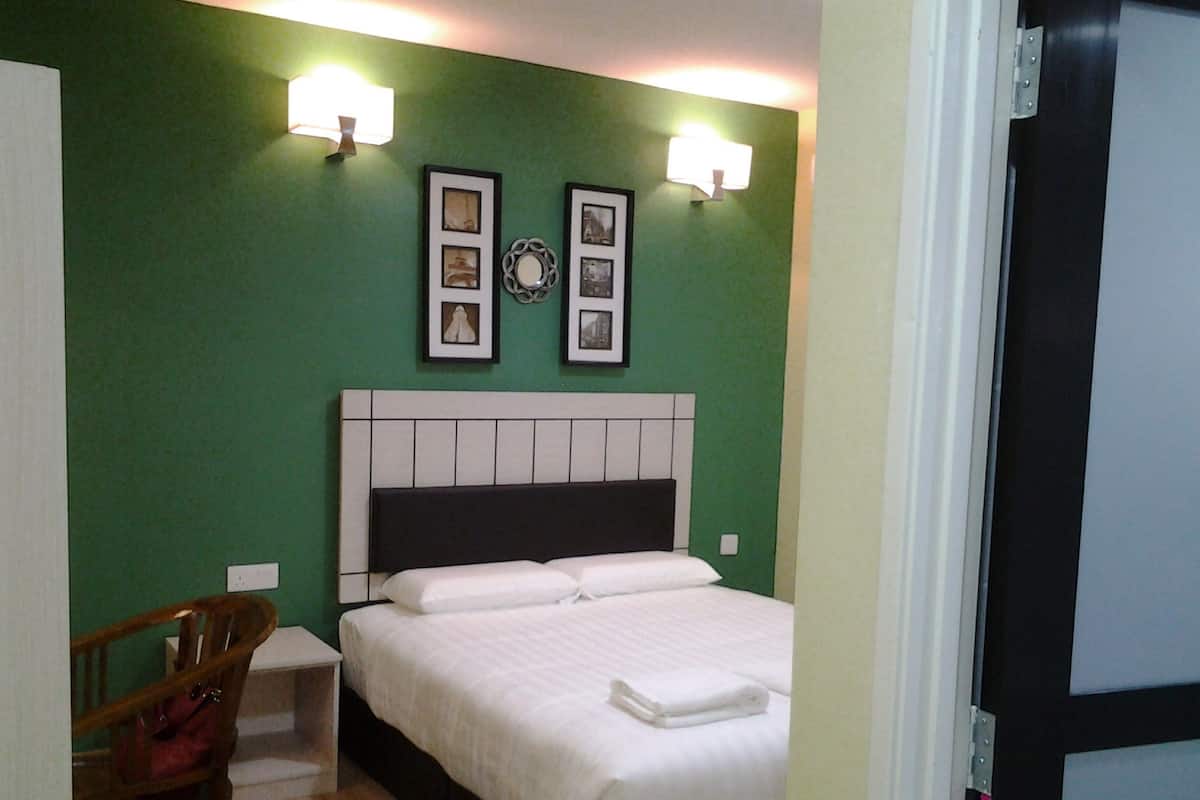 A hotel room with a bed, a chair, a nightstand, and wall-mounted lights.