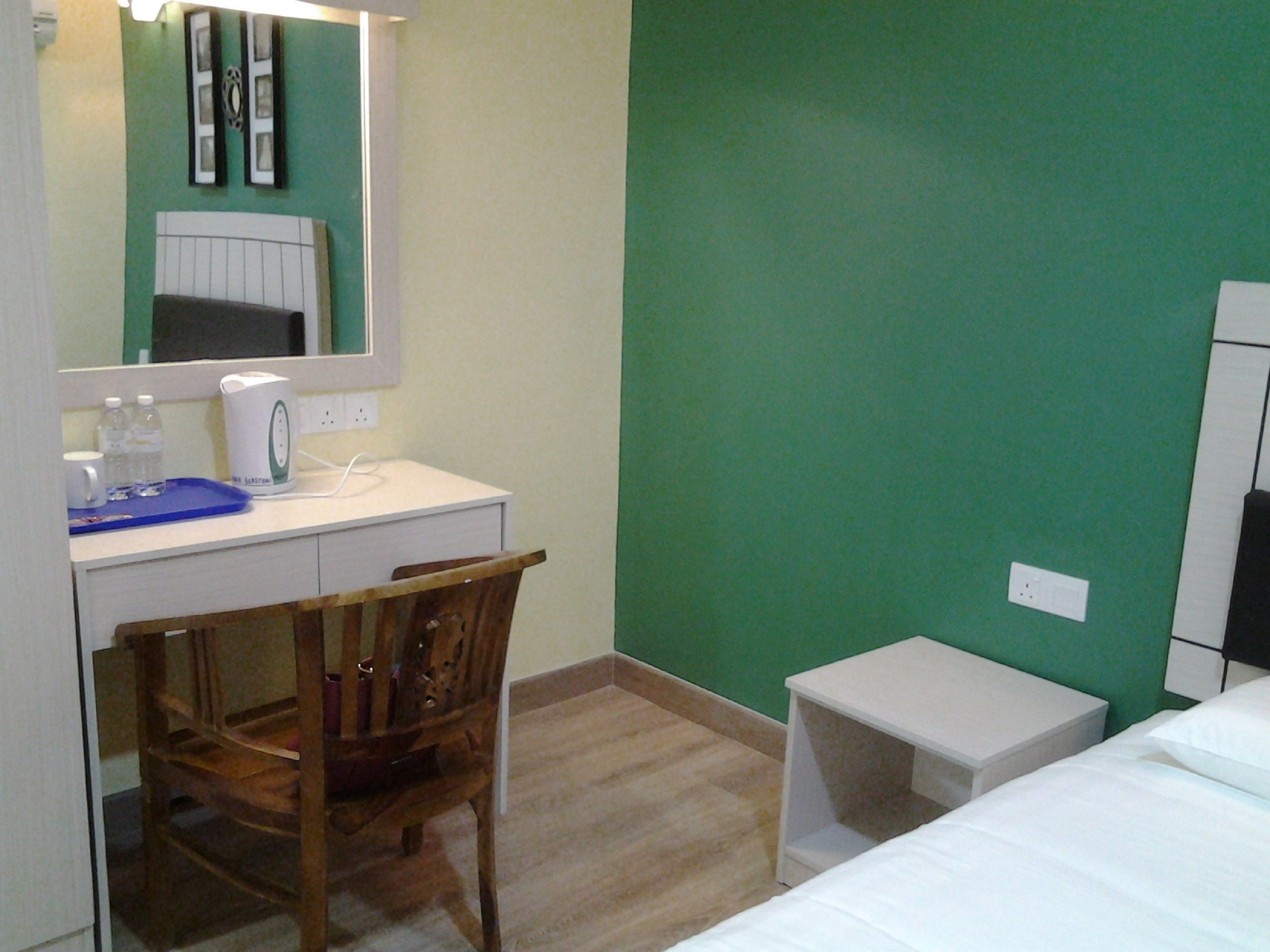 A hotel room with a wooden chair, a desk with a white kettle, a small white table, and a bed.