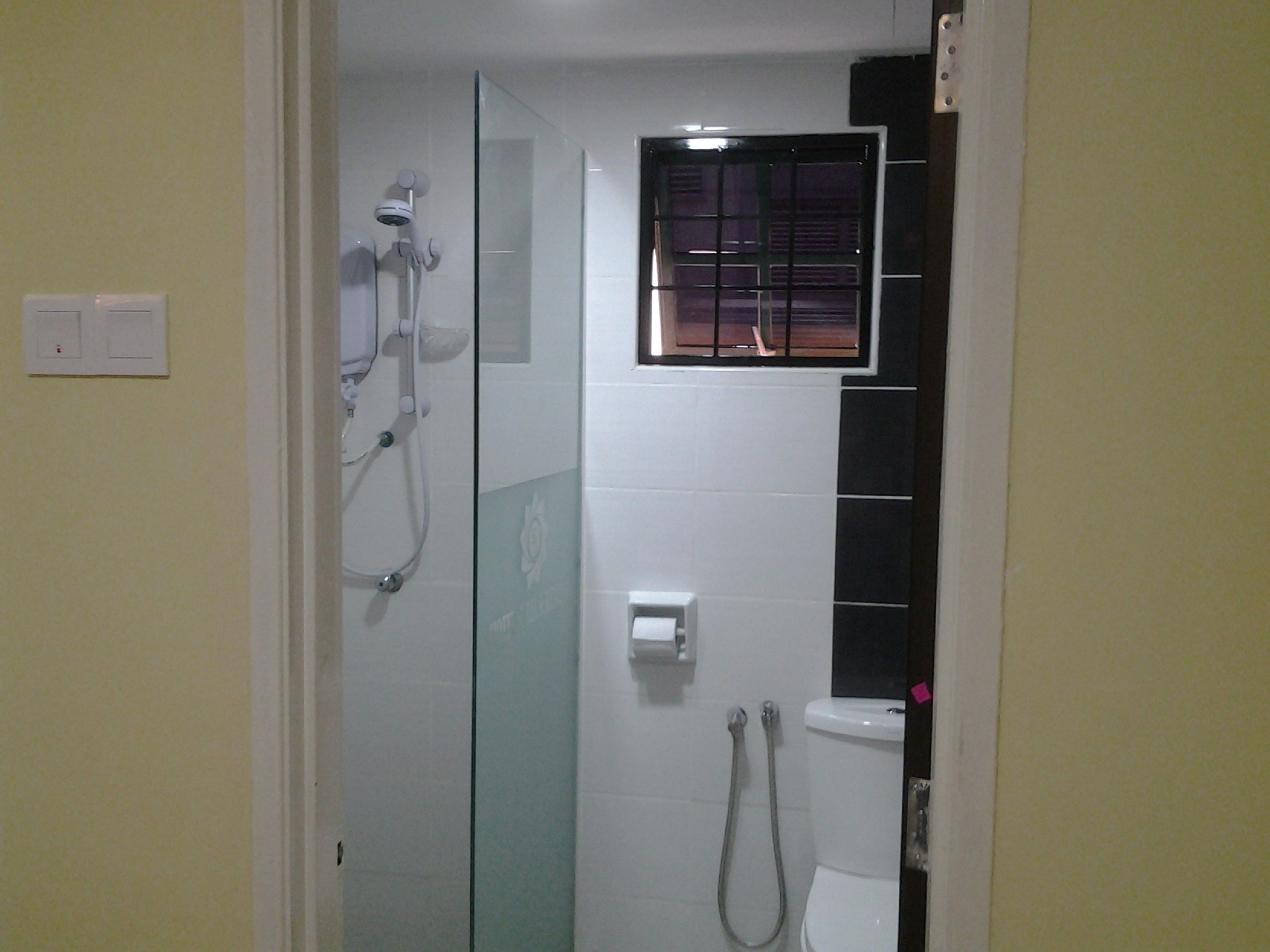 A bathroom with a glass shower enclosure, a toilet, and a small window.