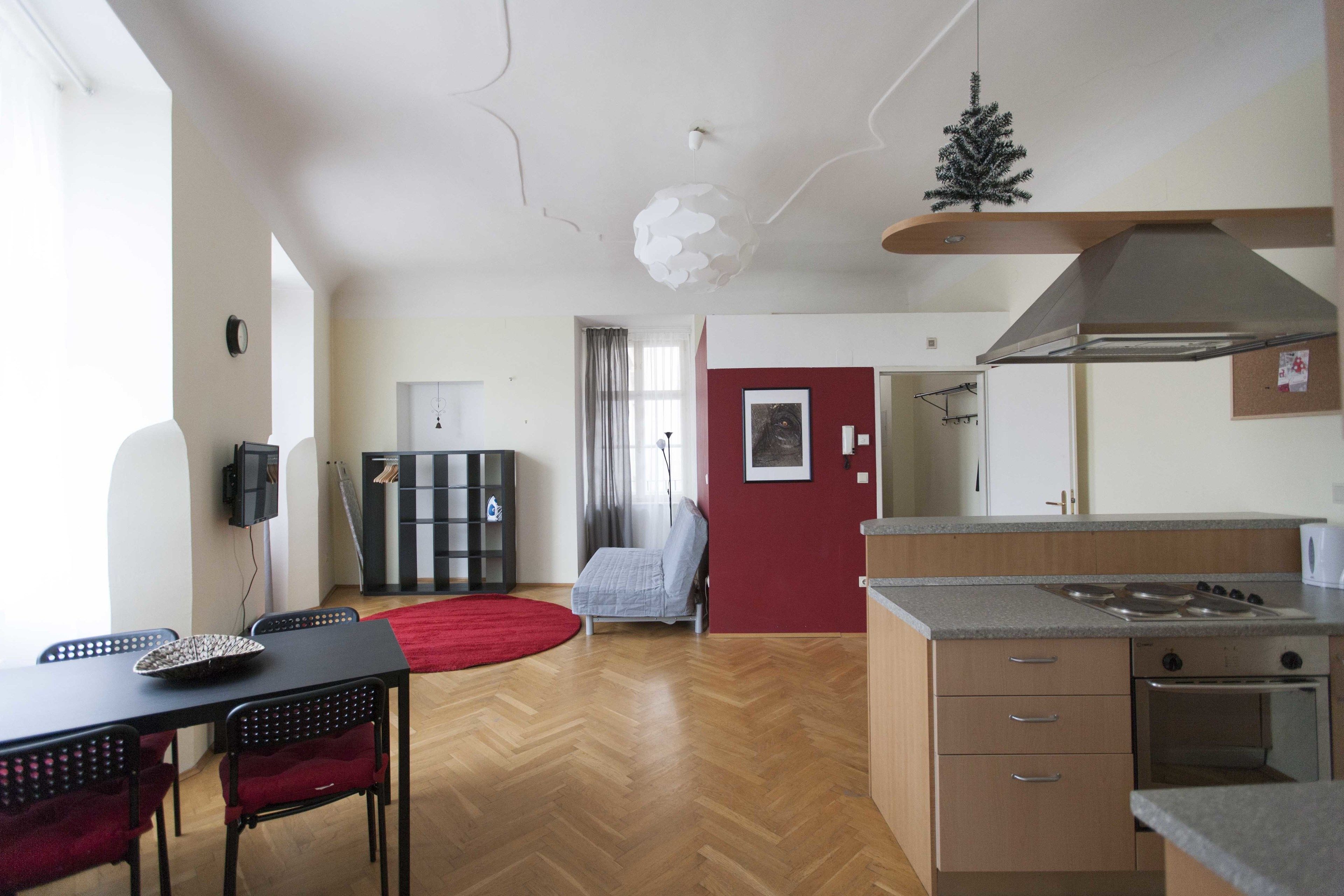 A modern kitchen with a stove, oven, and a red wall. There is a dining area with a table and chairs.
