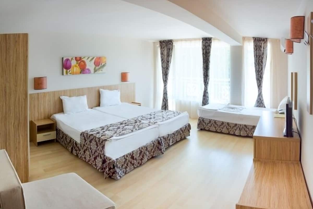 Una habitación de hotel moderna con una cama grande, una cama más pequeña, un escritorio y una ventana con cortinas.