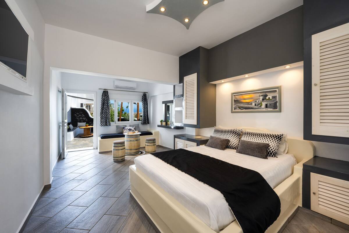 A modern bedroom with a large bed, a desk, and a chair. There is a window with a view of the outside.