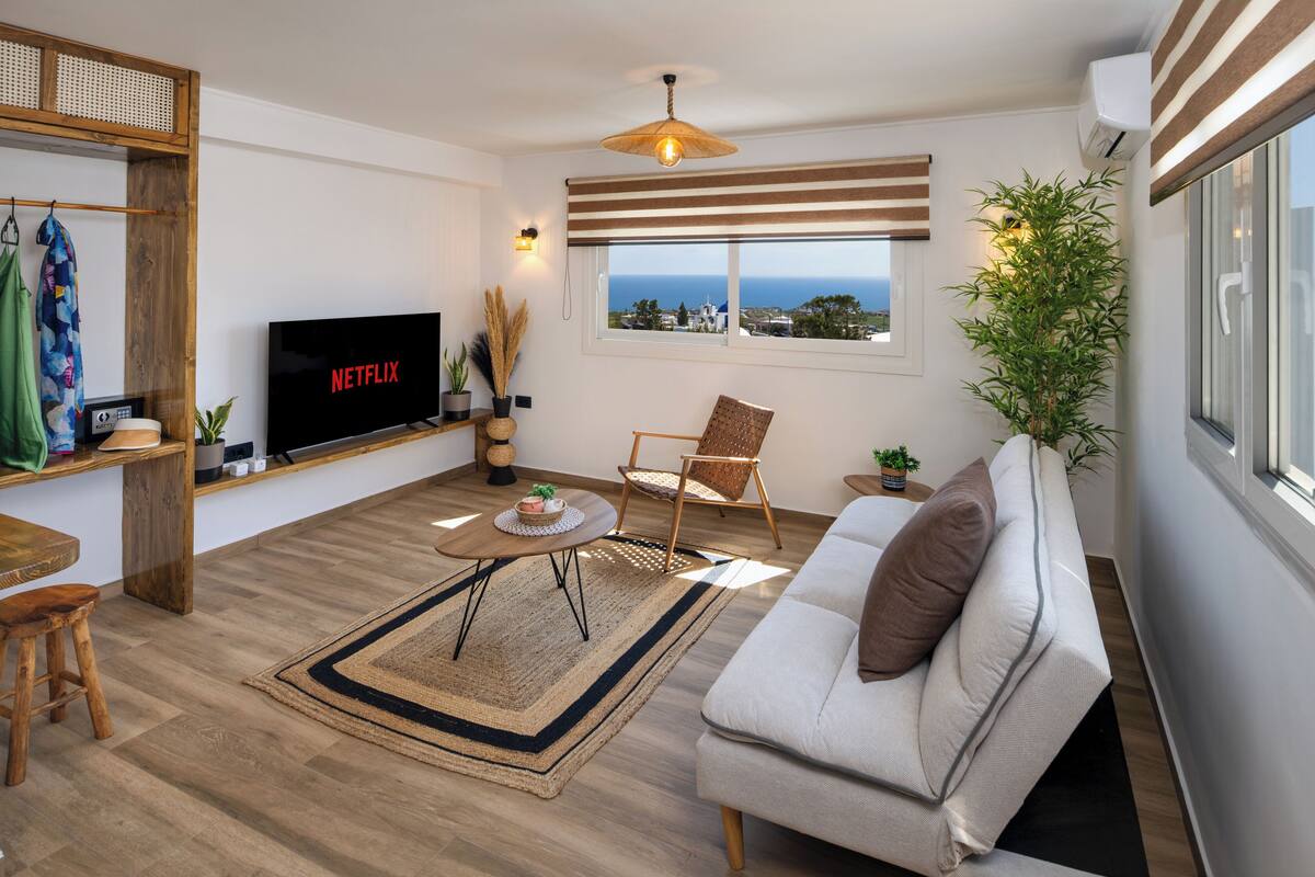 A modern living room with a flat-screen TV, a sofa, a coffee table, and a view of the sea.