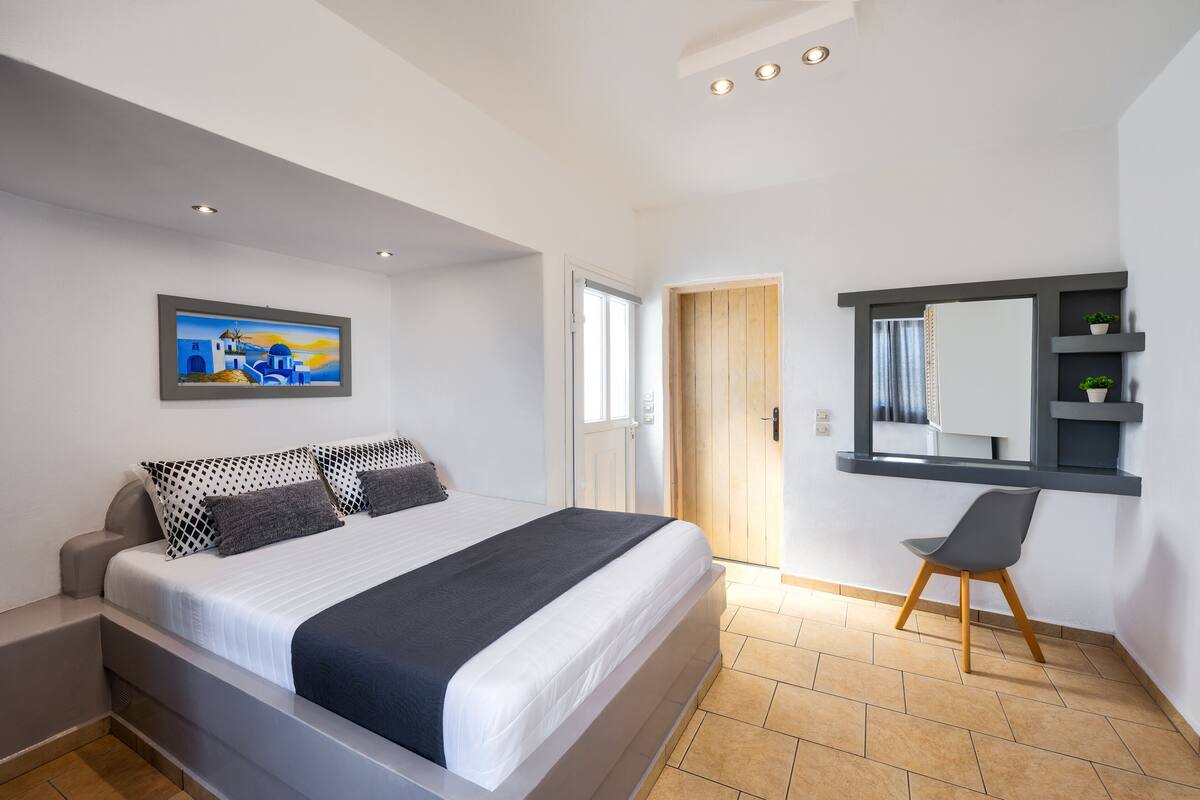 A bedroom with a bed, a chair, a painting, a door, and a mirror.
