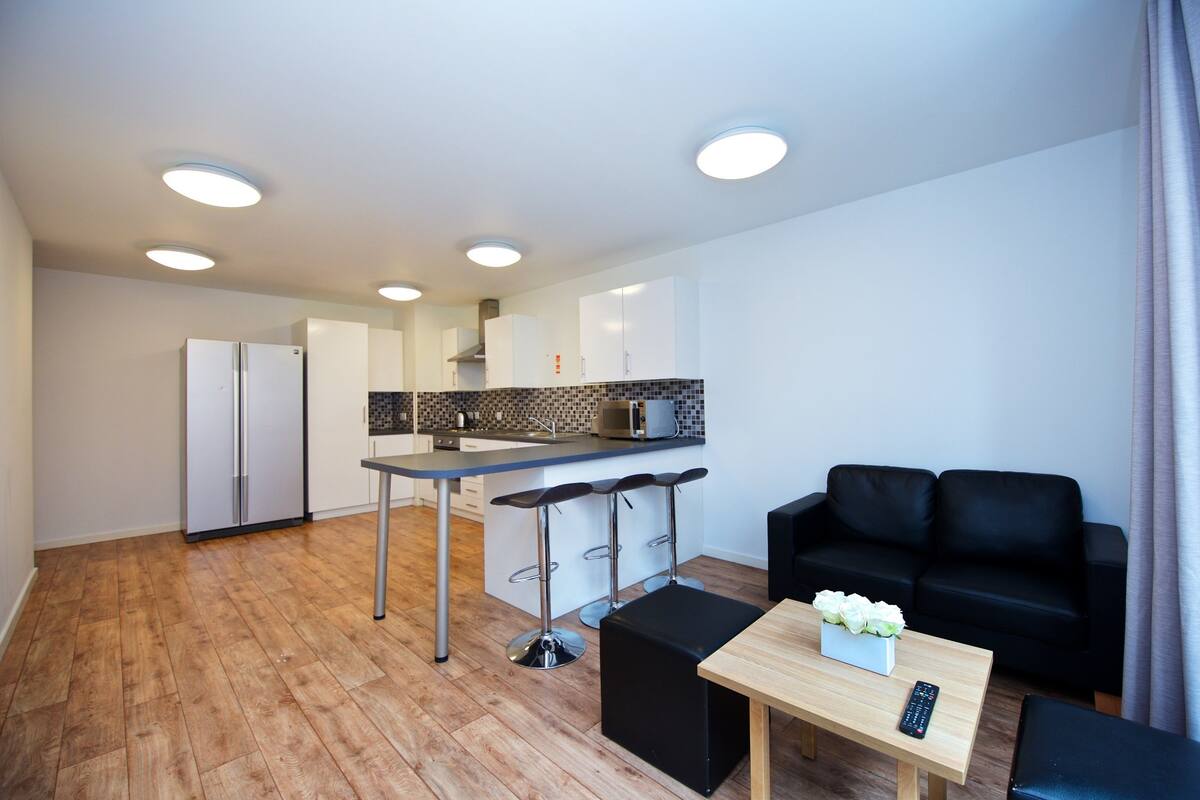 A modern kitchen with a central island, a dining area with a table and chairs, and a black sofa in a living area.