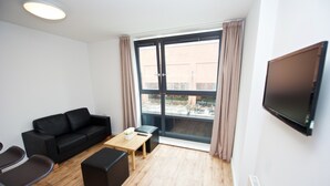 A modern living room with a black leather sofa, a wooden coffee table, and a TV mounted on the wall. - CityLiveIn London Wembley (Wembley)