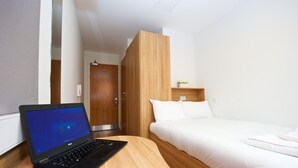 A hotel room with a wooden desk, a laptop, a bed, and a small shelf with a plant. - CityLiveIn London Wembley (Wembley)