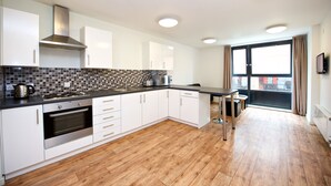 A modern kitchen with white cabinets, a tiled backsplash, and a wooden floor. - CityLiveIn London Wembley (Wembley)