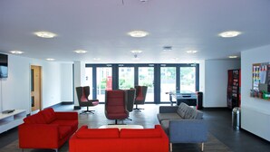 A modern waiting area with red and grey sofas, a coffee machine, and a vending machine. - CityLiveIn London Wembley (Wembley)