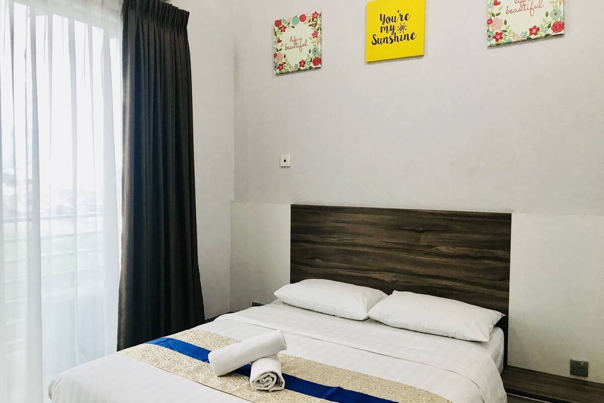 A neatly made bed with white linens and a blue accent, a wooden headboard, and two motivational wall decorations.