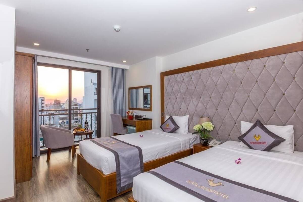 A hotel room with two beds, a desk, a chair, and a large window with a city view.