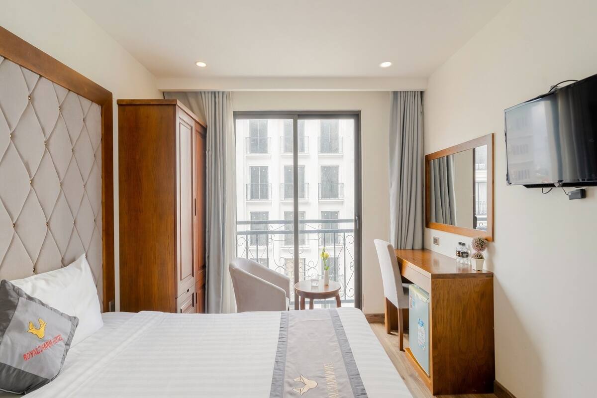 A hotel room with a bed, a desk, a chair, a television, and a balcony with a view of buildings.