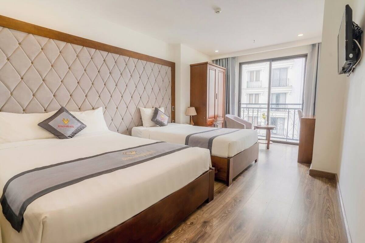 A hotel room with two beds, a large window, a wardrobe, and a small table.
