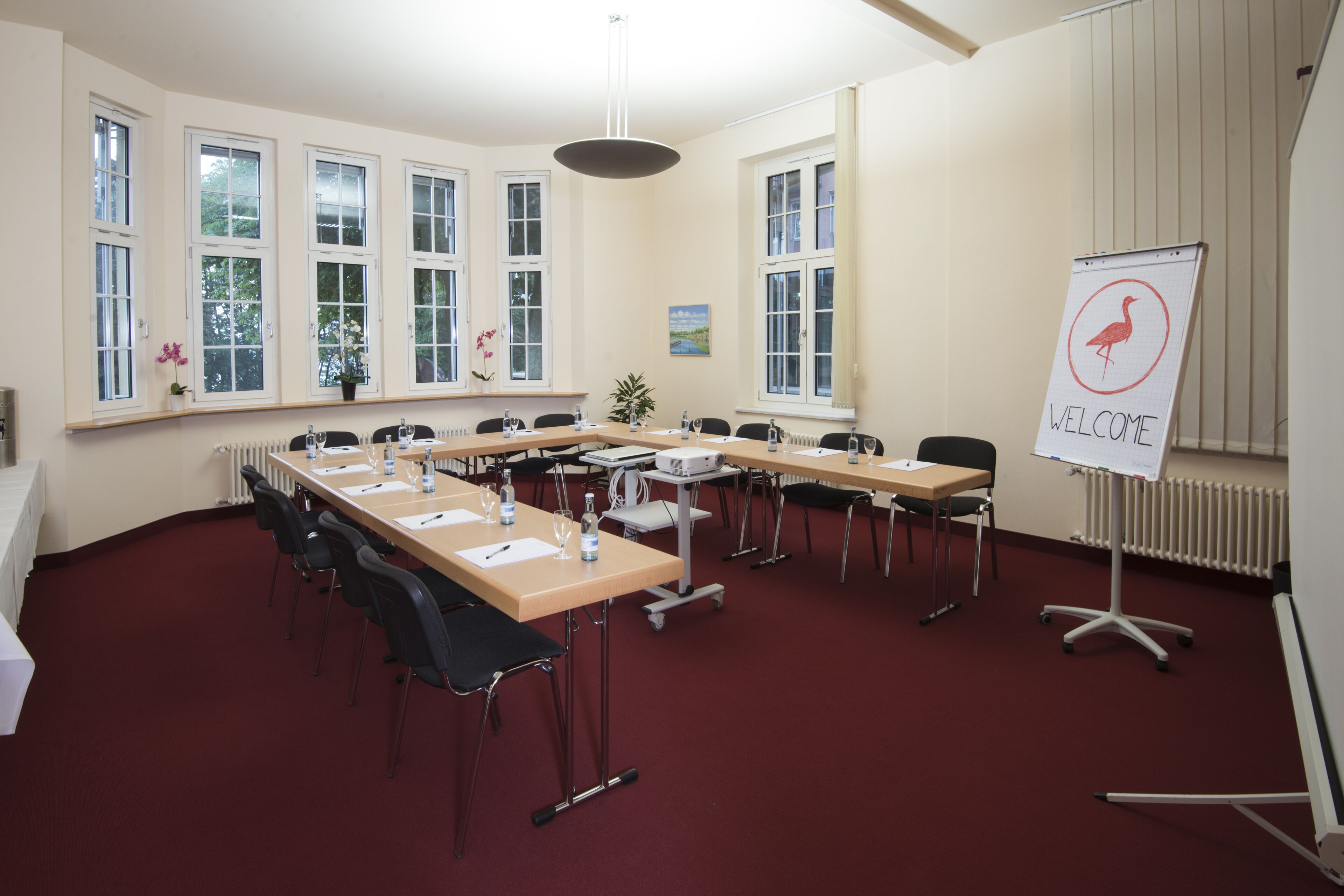 A conference room with a long table, chairs, a projector, and a whiteboard with a 'Welcome' sign.