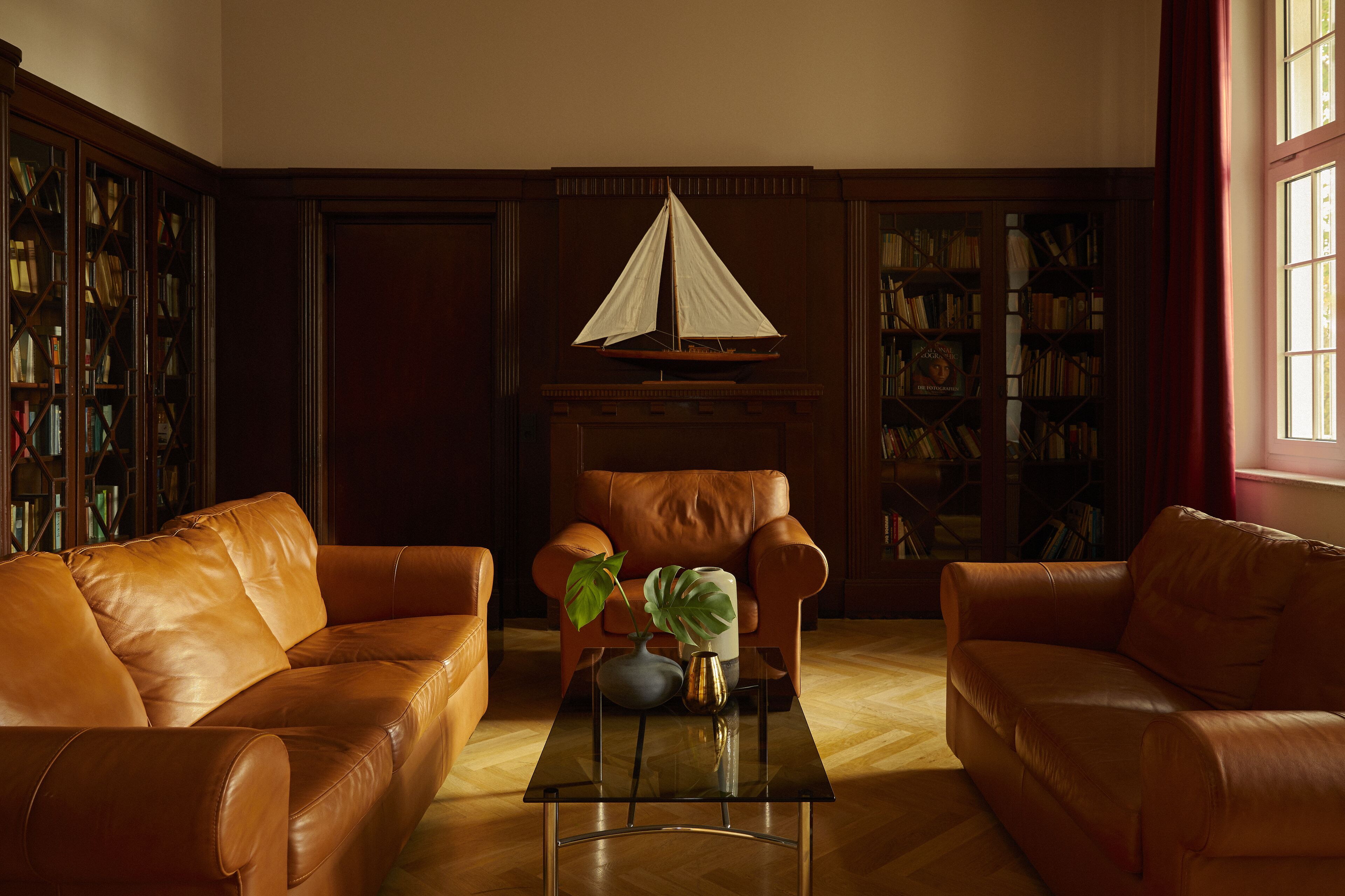 A room with two leather sofas, a glass coffee table, a bookshelf, and a decorative sailboat.